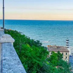 Coastal town with a lighthouse and buildings overlooking the blue sea, with a walkway in the foreground.