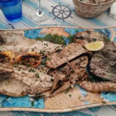 A platter of grilled fish and shrimp with lemon wedges and parsley.