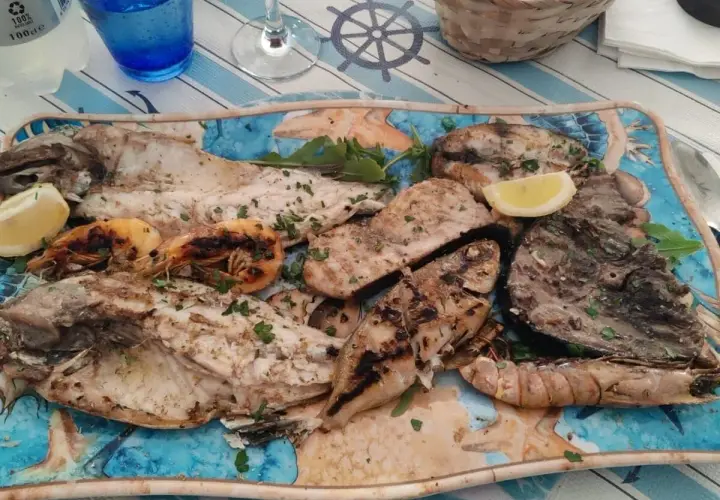 A platter of grilled fish and shrimp with lemon wedges and parsley.