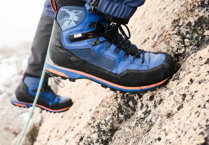 Close-up of a blue and black hiking boot with orange accents on a rocky surface.