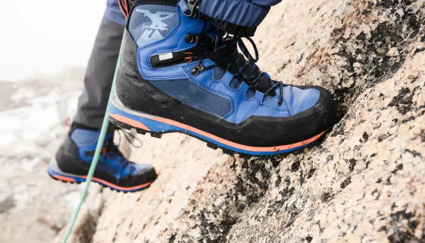 Close-up of a blue and black hiking boot with orange accents on a rocky surface.