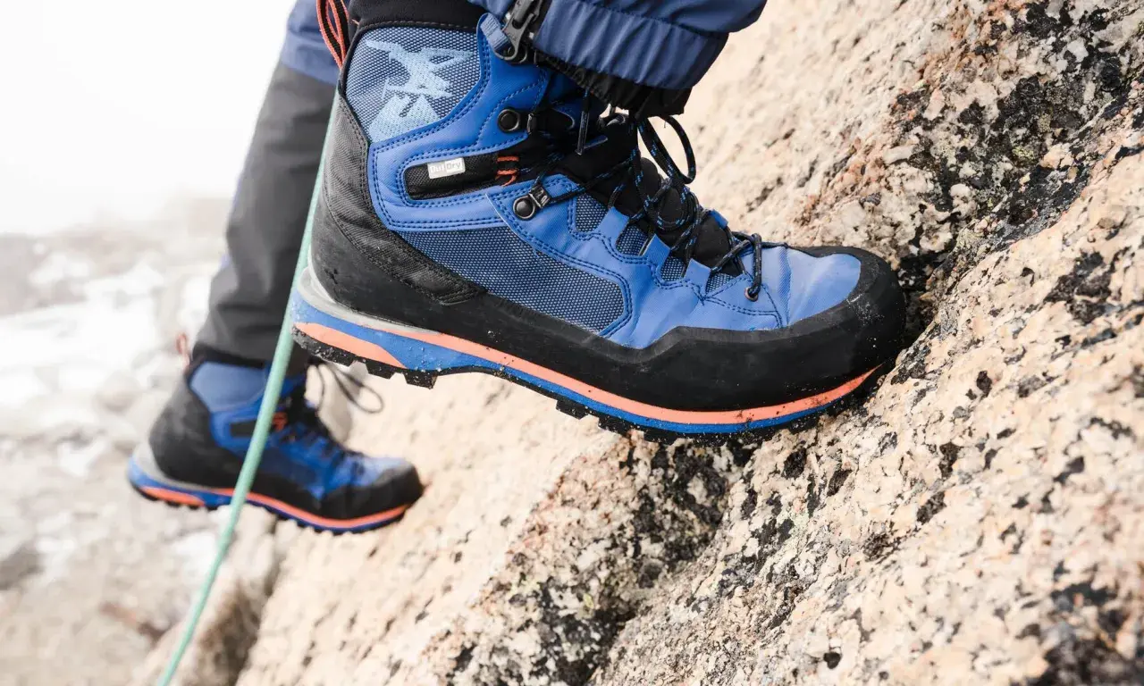 Close-up of a blue and black hiking boot with orange accents on a rocky surface.