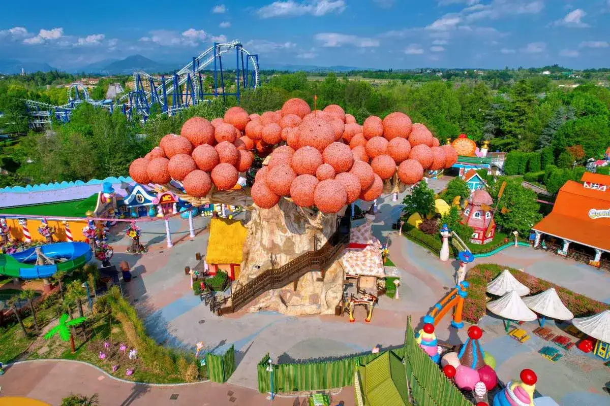 Un'attrazione di Gardaland 2026 con un albero gigante e colorato, montagne russe e giochi per bambini.