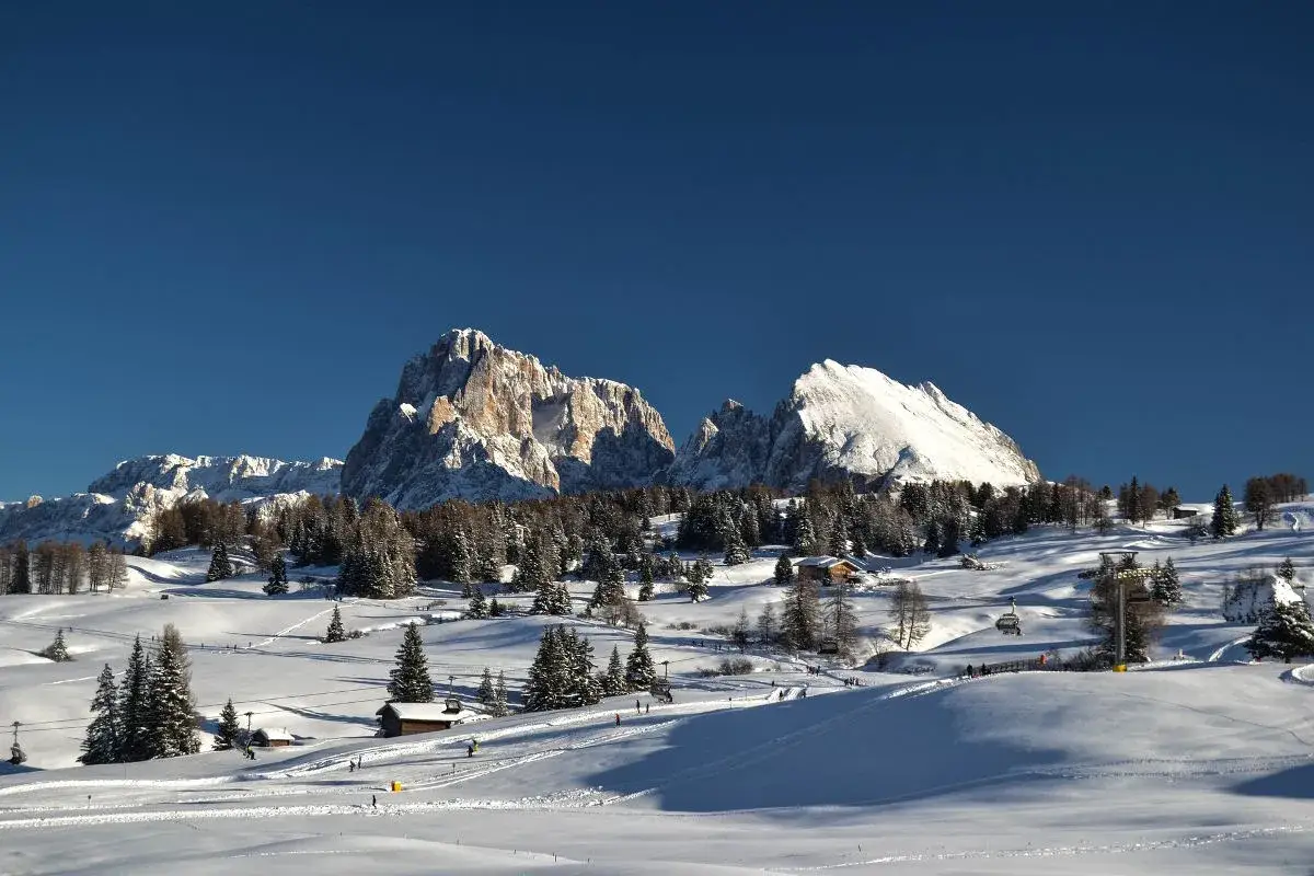 Paesaggio invernale con montagne innevate, boschi di abeti e piste da sci. La neve in montagna brilla sotto il cielo azzurro.